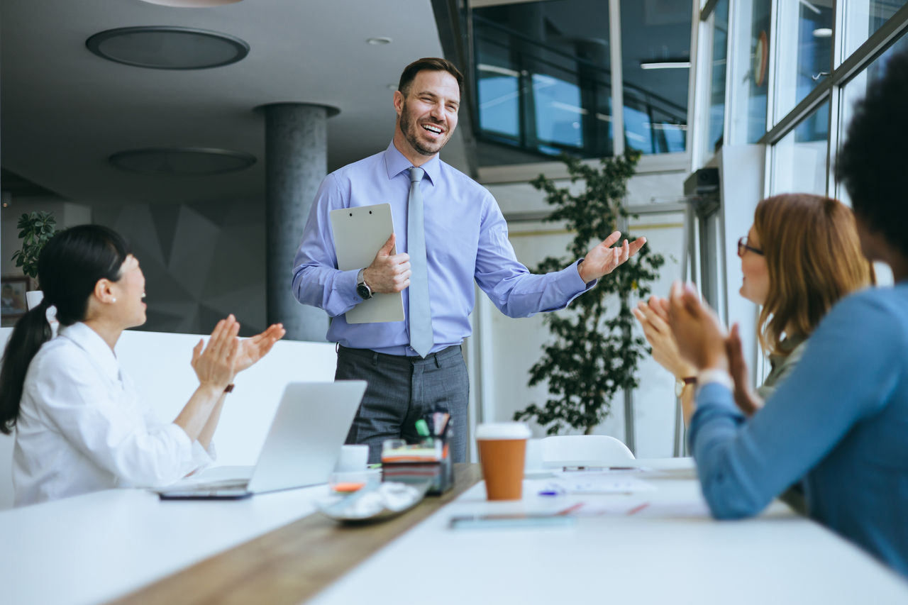 During a business presentation, an employee is being applauded by his team in an office setting, which encourages business teamwork and success