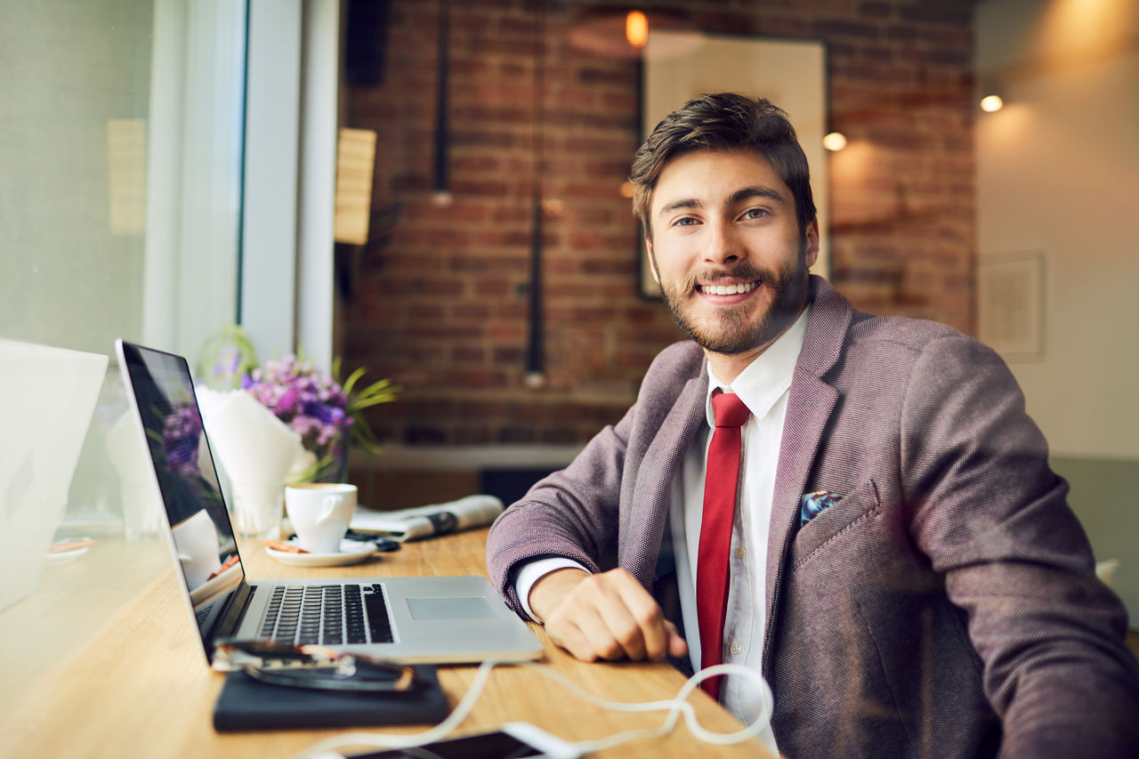 Confident young freelancer sitting at table and staring straight at camera in a cafe