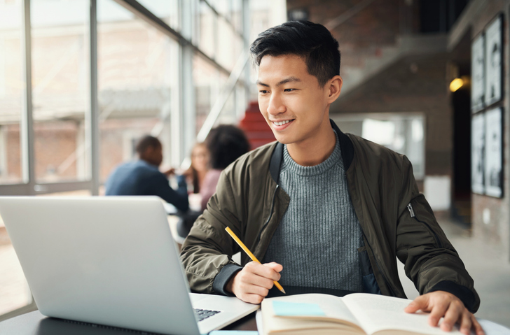 College student, asian man and studying on laptop at campus, research and education test, exam books and course project. Happy Japanese university student, knowledge and learning online technology